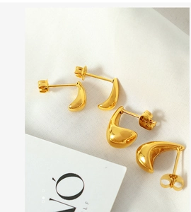 Detail view of four minimalist gold teardrop earrings on white textured fabric background
