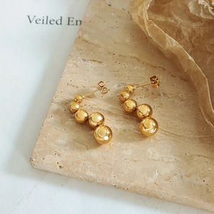 Gold stainless steel beaded arc earrings on marble stone background with warm lighting