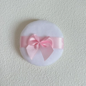 Close-up of a round white velvet makeup puff with a delicate pink satin bow decoration