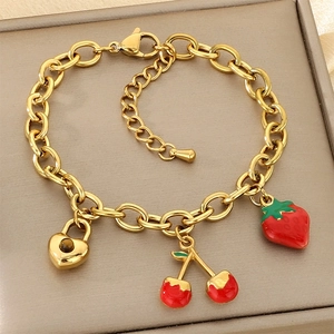 Détail d'un bracelet doré avec pendentifs cadenas cœur, cerises et fraise rouge