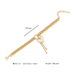 Macro detail of gold stainless steel Cuban chain necklace with heart and bead tassel