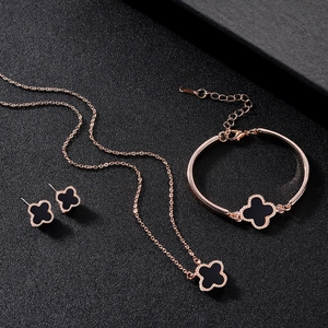 Rose gold jewelry set with black clover motifs displayed on a black textured surface