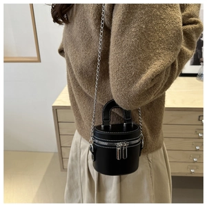 Détail d'un mini sac seau noir avec surpiqûres blanches et bandoulière chaîne sur modèle