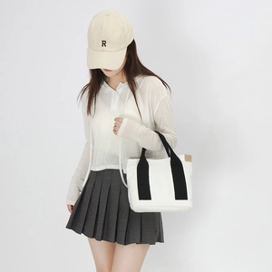 Close-up of white canvas tote bag with black handles on model in casual outfit
