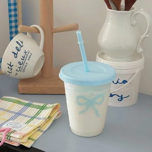 Close-up of clear plastic straw cup with blue bow pattern and matching lid in home setting