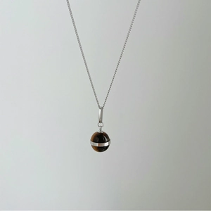 Detail shot of a tiger eye spherical pendant with a polished silver chain necklace