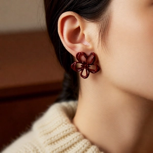 Close-up of deep red hollow flower earrings worn by a model in warm lighting