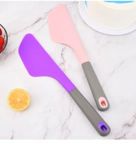 Pink and purple large silicone spatulas with grey handles for baking on marble surface