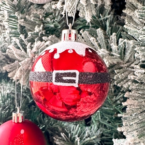 Close-up of red Christmas ball with Santa belt design on a snowy green pine tree