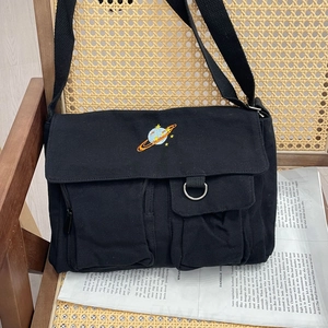 Close-up of black canvas messenger bag featuring colorful planet embroidery and pockets