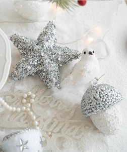 Detailed view of silver star, bird and acorn Christmas tree ornaments on white snowy background