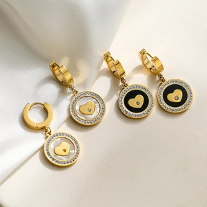Golden heart earrings with white shell and black onyx dangles on beige background