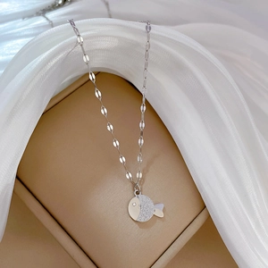 Macro detail of a silver fish pendant encrusted with clear stones on beige jewelry box