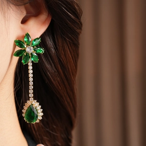 Close-up of elegant gold drop earrings with green zircon flowers and teardrop crystals