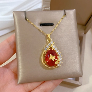 Close-up of a gold necklace featuring a teardrop red gemstone with clear zircon pavé