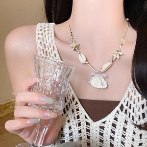 Detail of starfish and shell charms on a gold chain necklace worn by a model