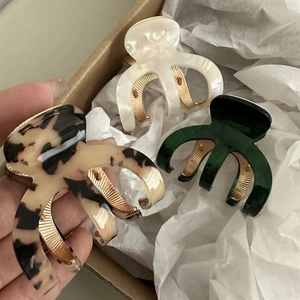 Three acetate hair claw clips in tortoiseshell, pearl white, and dark green finishes