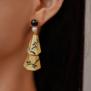 Close-up of gold geometric drop earrings with black branch patterns on a female model