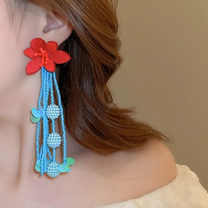 Detailed close-up of beaded tassel earrings with red flower and blue fringe beads