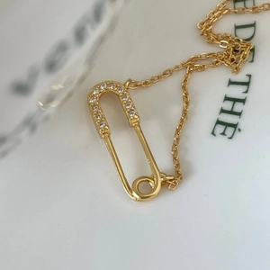 Macro shot of gold safety pin pendant with micro-pave crystals on thin O-chain necklace