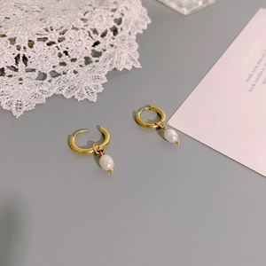 Minimalist gold hoop earrings with natural pearls on a white lace and card background