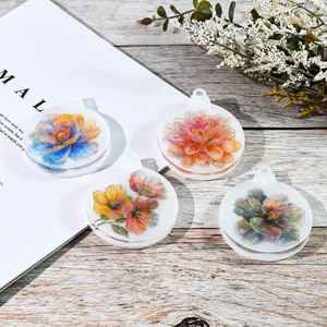 Detailansicht von vier runden Blumen-Resin-Anhängern mit diversen Mustern auf Holzoberfläche