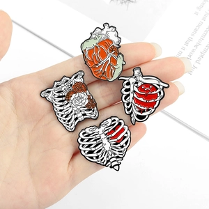 Handheld display of four anatomical enamel pins featuring hearts and floral rib cages