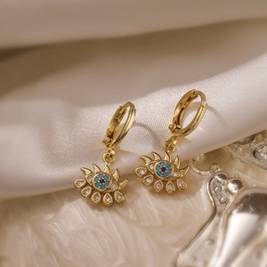 Gold plated evil eye hoop earrings with blue zircon insets on white silk fabric