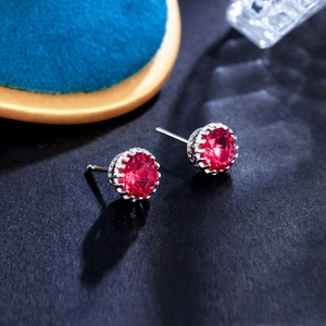 Macro shot of 8mm round-cut ruby red zircon earrings with classic silver six-claw setting