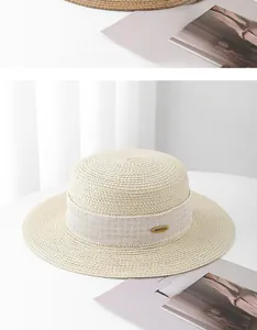 Detailed close-up of straw sun hat featuring a white woven band and gold metal logo charm