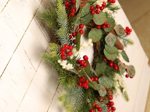 Close-up of Christmas wreath with red berries and pine cones on white rustic wood