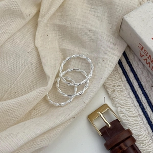 Close-up of three 925 sterling silver twist rings on a beige linen fabric background