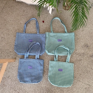Flat lay of blue and green checkered canvas tote bags in small and large sizes on stone floor