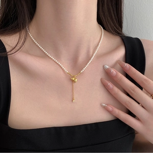 Détail du collier de perles avec pendentif gourde dorée et pompon porté par un mannequin