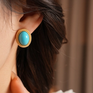 Close-up of vintage style oval turquoise earring with gold rope texture worn by model