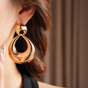 Detail of gold teardrop hollow earrings on model with polished metallic finish