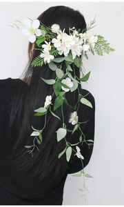 Detail of white artificial flowers and green vine hairpiece on dark hair for bridal style