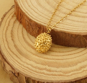 Detail of 18k gold plated stainless steel durian pendant on natural wood background