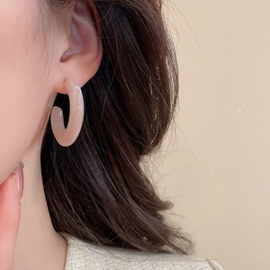 Détail des boucles d'oreilles créoles C en acrylique rose avec texture marbrée sur modèle