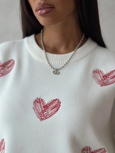 Detailed close-up of ribbed crewneck and red heart embroidery on white knit sweater