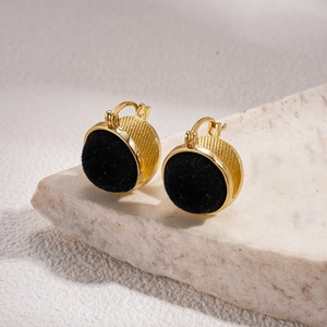 Detail of gold circular earrings with black velvet inlay on beige marble stone