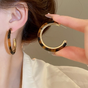 Detail view of large C-shaped amber resin earrings with elegant gold metallic accents
