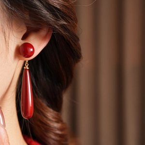 Detail of dark red teardrop earrings with gold accents worn by a model in close-up
