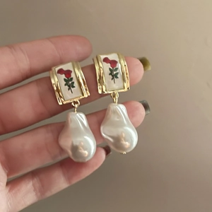 Detail of vintage gold earrings with red rose pattern and white baroque pearl drops