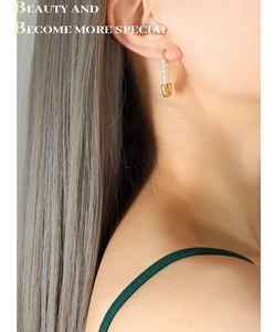Close-up of golden paperclip earrings with pearl accents worn by a model in soft light