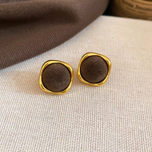 Detailed view of brown velvet round pendant earrings with gold metal frame on beige fabric