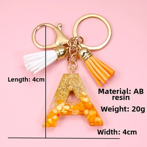Close-up of resin letter A keychain with orange stone chips, gold foil, and double tassels