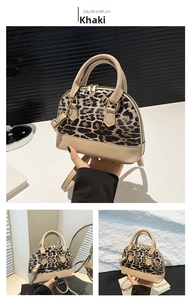 Detail view of khaki leopard print shell bag featuring a leather handle and metal zipper