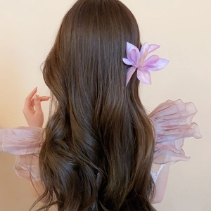 Detailed view of a purple fabric hibiscus flower hair clip on wavy brown hair