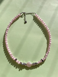 Detail of pink cat-eye bead necklace featuring a central white pearl and silver lobster clasp